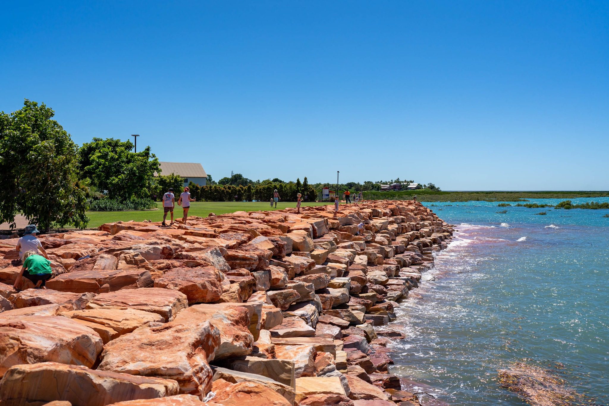 The Town Beach foreshore in Broome, which has a well-maintained green lawn behind a bank of red rocks that hold back the ocean water